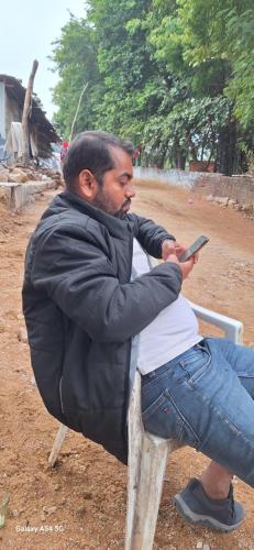 un hombre sentado en un banco sosteniendo un celular en The Golden Palm Khajuraho, en Khajurāho
