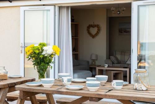 uma mesa de madeira com tigelas azuis e brancas e um vaso de flores em Sound of the Sea, beach front Bungalow with hot tub, in Tywyn em Tywyn