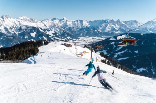 zwei Personen, die auf einer schneebedeckten Skipiste Ski fahren in der Unterkunft Loftwohnung mit Bergblick in Saalfelden am Steinernen Meer