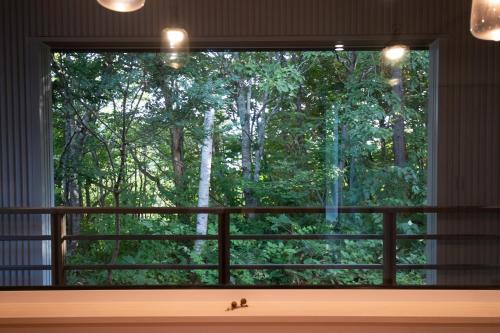 a window with a cat sitting on a window sill looking out at trees at ユニテ蔵王ジョーニダ リゾート in Yamagata