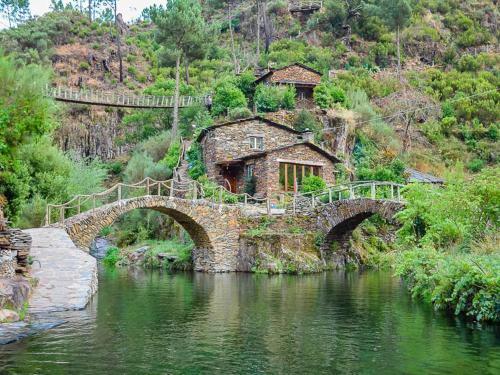 a bridge over a river with a building on a hill at Casa Raposo in Miranda do Corvo
