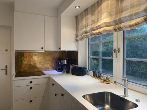 uma cozinha com armários brancos, um lavatório e uma janela em Hüs Claire em Kampen