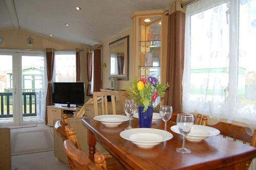 a dining room with a table with glasses and flowers on it at Caravan 251 Bryn Y Mor Beach Side Park in Tywyn