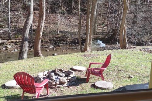 two red chairs sitting next to a fire pit at Quaint Cabin By The Creek Private in Pipestem