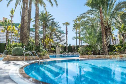 una piscina con palmeras en un complejo en AR Diamante Beach & SPA Hotel 4 SUP, en Calpe