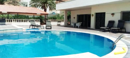 a large blue swimming pool with chairs and a house at Musharbash in Al Baḩḩāth