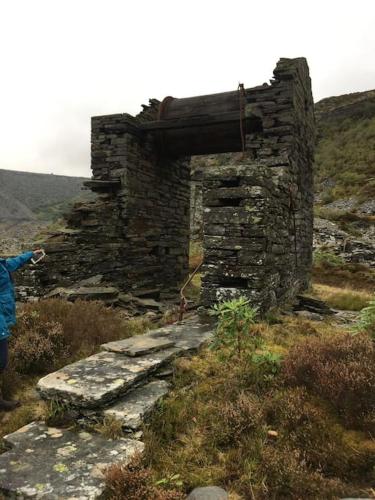 a person standing next to an old stone building at Cosy terrace cottage built into the mountain side. in Blaenau-Ffestiniog