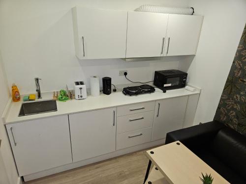 a small kitchen with white cabinets and a microwave at London Glamour Apartments in London
