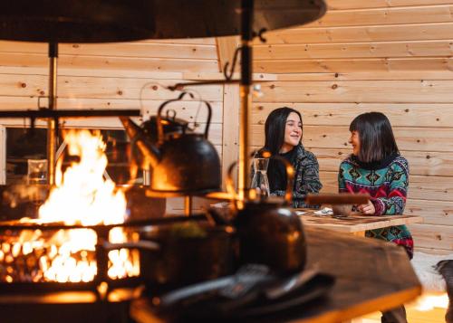 Due donne sedute a un tavolo di fronte al fuoco di Nova Galaxy Village a Rovaniemi