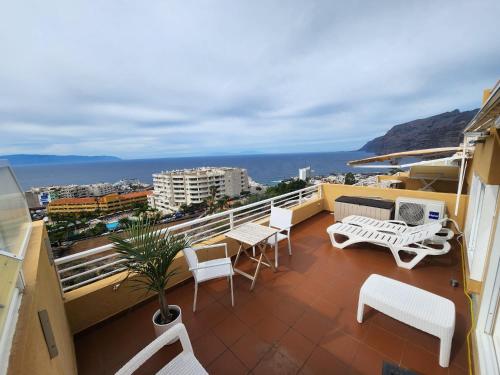 a balcony with white chairs and tables on a building at Los Gigantes,huge terrace,sea view,air conditioning in Puerto de Santiago