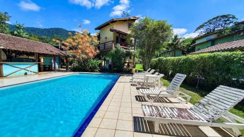 a swimming pool with lounge chairs and a house at Hotel e Pousada Canto Mágico in Maresias