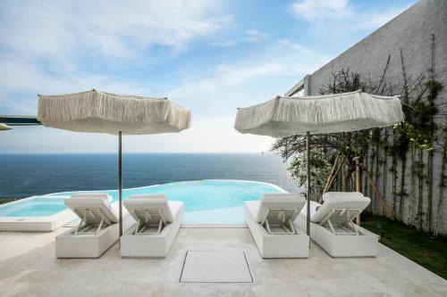 a pool with chairs and umbrellas and the ocean at Private Jet Villa Uluwatu in Uluwatu