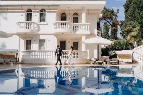 a bride and groom walking in front of a white mansion at Ostrova Spa Hotel in Sochi
