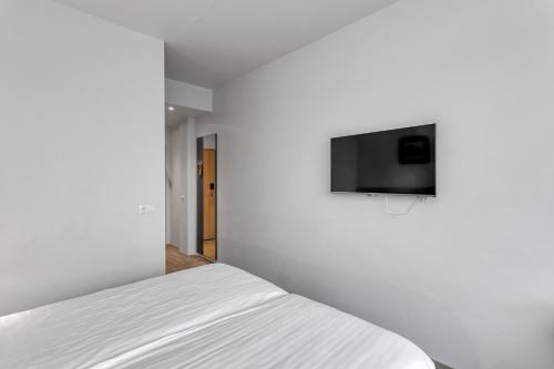 a white bedroom with a bed and a tv on the wall at Hotel Vellir in Hafnarfjördur