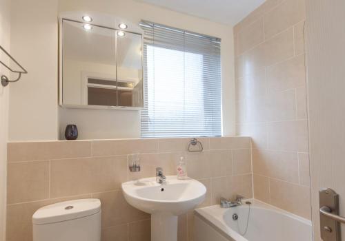 W łazience znajduje się umywalka, toaleta i lustro. w obiekcie Logie Green Road Apartment w Edynburgu