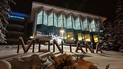 um edifício na neve com bancos à sua frente em Interhotel Montana em Spindleruv Mlyn