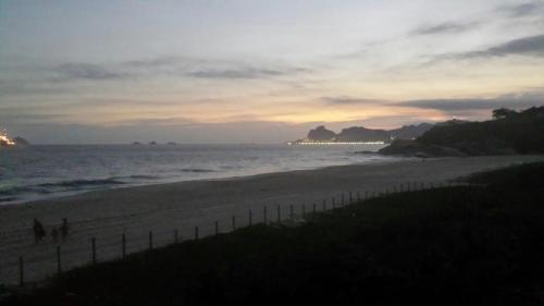 a beach at sunset with people walking on the sand at Casa confortável in Niterói