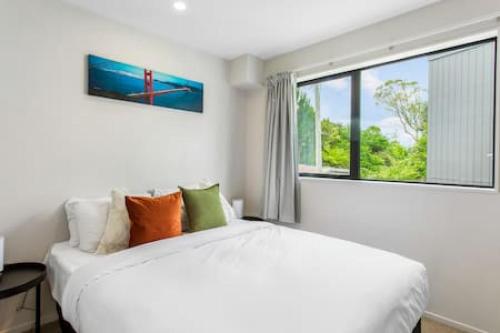 a white bedroom with a large bed and a window at Urban Pulse Townhouse with parking in Auckland