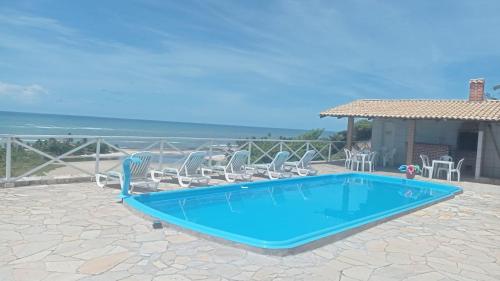 a swimming pool with chairs and the ocean in the background at Pousada Portal dos Coqueirais in Jequia da Praia