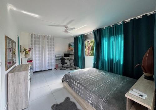 Schlafzimmer mit einem Bett mit blauen Vorhängen und einem Schreibtisch in der Unterkunft Spacieux haut de villa avec terrasse et jardin in Les Abymes
