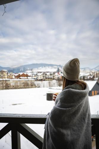 a woman in a blanket looking out of a window at a snow covered city at Zatyshok nad Prutom in Bukovel
