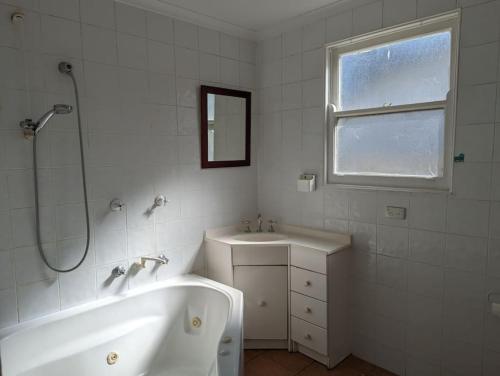 Baño blanco con bañera y lavamanos en Comfortable Home 3bdr Nr Kingston and Fyshwick en Fyshwick