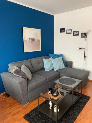uma sala de estar com um sofá cinzento e uma parede azul em Fehmarn-OstseeferienMöwennest 205 em Burgtiefe auf Fehmarn 