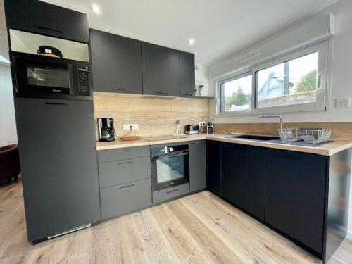 une grande cuisine avec des placards noirs et un four micro-ondes dans l'établissement Maison rénovée 6 pers, centre Quiberon, jardin, proche plage et commerces - FR-1-478-264, à Quiberon