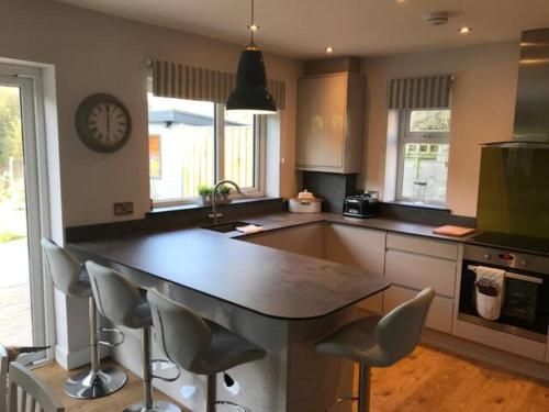 a kitchen with a counter with chairs and a clock at Just Stay Wales - Marshmallow Cottage, Oxwich in Swansea