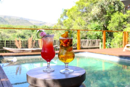 two cocktails sitting on a table next to a swimming pool at Barefoot Addo Elephant Lodge in Addo