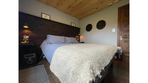 1 dormitorio con cama blanca y cabecero de madera en Cabaña - Granja Lago Frío, en Coyhaique