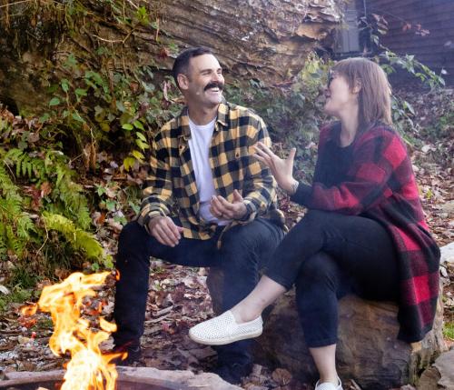 a man and a woman sitting next to a fire at Tiny Cabin in RRG - The Naturalist in Rogers