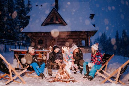 a group of people sitting around a fire in the snow at Legenda Lasu - drewniany domek w górach z jacuzzi, przy stoku narciarskim Kotelnica, Białka Tatrzańska, w pobliżu Term Bania in Groń
