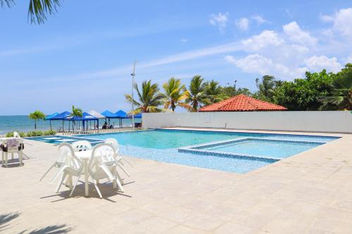a swimming pool with white chairs and the ocean at Magico Apartamento Frente al Mar 3 Habitaciones PV81 in Coveñas
