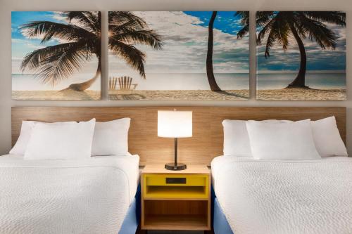 two beds in a hotel room with two palm trees at Days Inn by Wyndham Miami Airport North in Miami