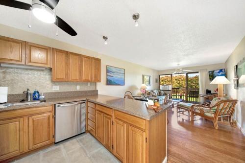 a large kitchen with wooden cabinets and a living room at Kauai Banyan Harbor B24 condo in Lihue