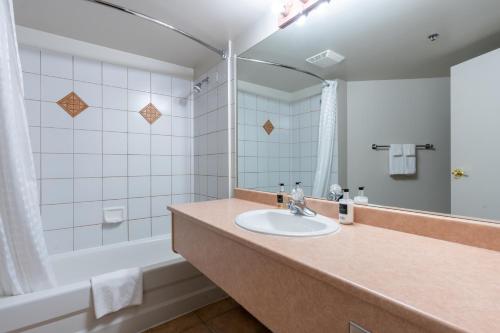 uma casa de banho com um lavatório, uma banheira e um espelho. em Sundance Lodge em Sun Peaks