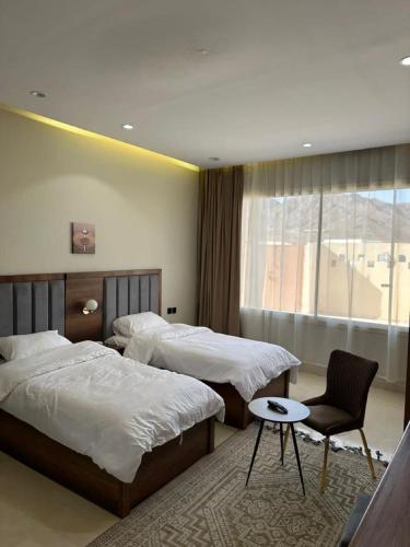 a bedroom with two beds and a chair and a window at أجنحة رونق العلا 2 in AlUla