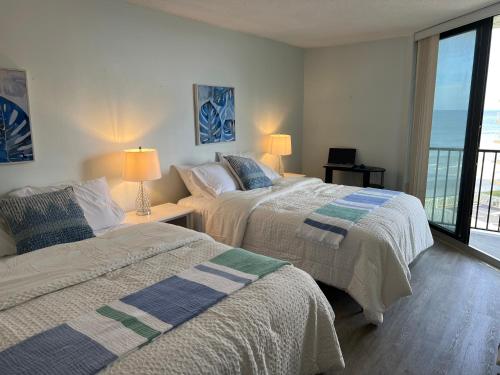 two beds in a bedroom with a view of the ocean at Coastal Condo on the beach at Ocean Trillium #501 in New Smyrna Beach
