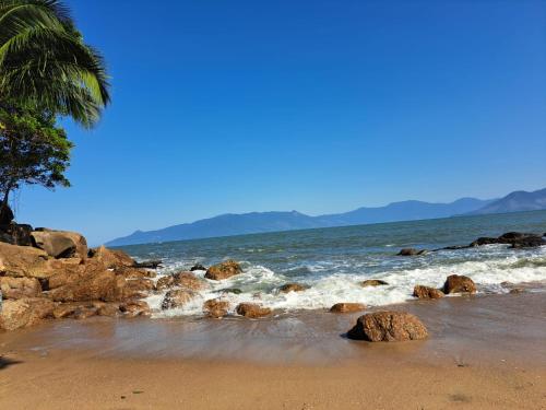einen Strand mit Felsen, einer Palme und dem Meer in der Unterkunft Chalé na Praia Martim de Sá in Caraguatatuba