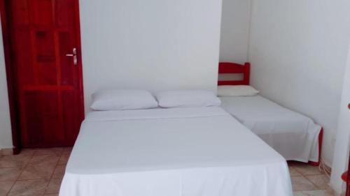 a room with two beds with white sheets and a red door at Pousada JK in Pirenópolis