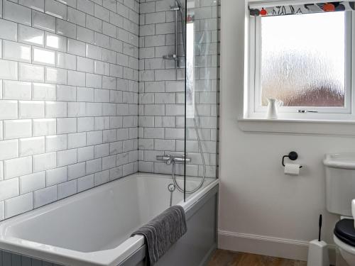 a white bathroom with a tub and a window at The Cottage in Leitholm