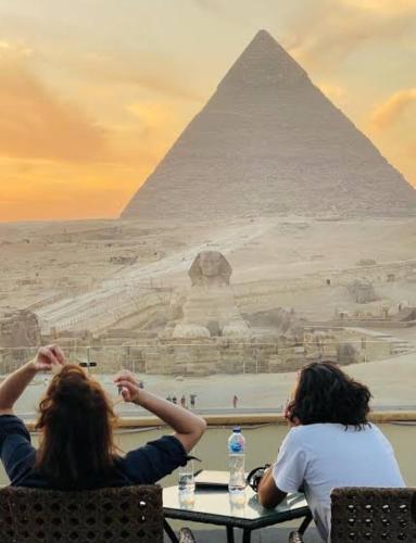 Royal pyramids residential في Ghaţāţī: يجلس شخصان على طاولة أمام الاهرامات