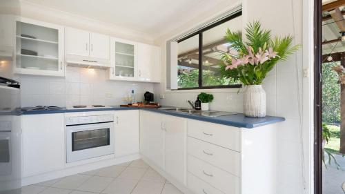 a kitchen with white cabinets and a vase with pink flowers at Sunrise Sands in Callala Beach