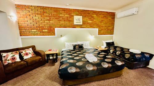a bedroom with a bed and a couch and a brick wall at Early Australian Motor Inn in Mildura