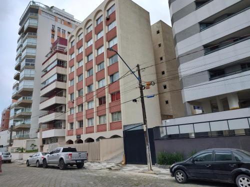twee auto's geparkeerd op een parkeerplaats naast hoge gebouwen bij Apartamento Caiobá Pé na areia. Quadra do Mar. in Matinhos