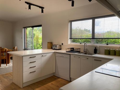 a kitchen with white cabinets and a sink and two windows at Family Adventure Get Away in Rotorua