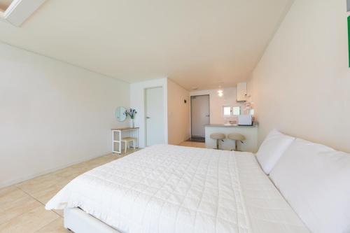a white bedroom with a white bed and a kitchen at Melodia Pension in Geoje 
