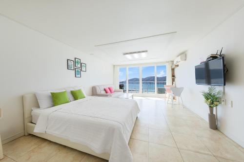 a white bedroom with a bed and a flat screen tv at Melodia Pension in Geoje 