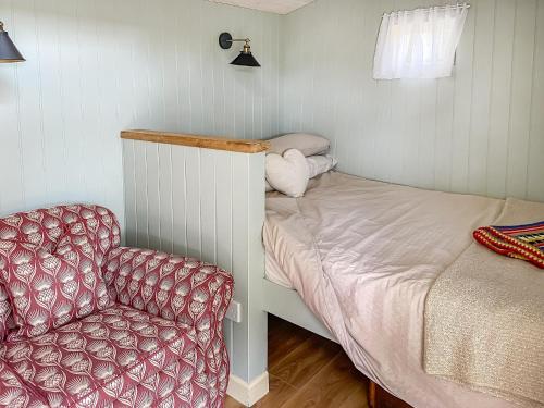 a small bedroom with a bed and a chair at Ivy Shepherds Hut - Uk45590 in Seend